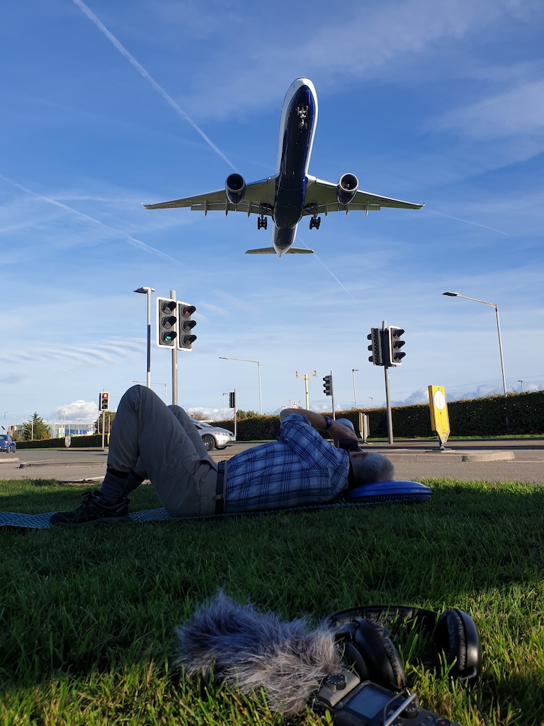 Stills photographer lies on the grass as jet plane comes in to lanc