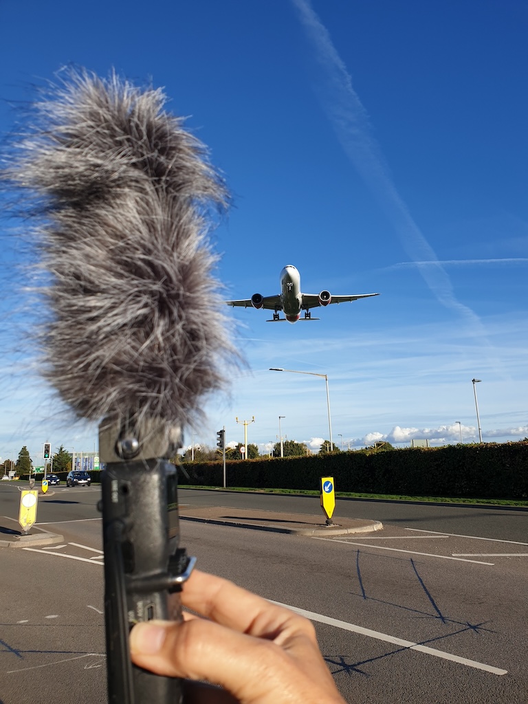 Stereo directional microphone with windgag being held up as jet plane comes in to lanc